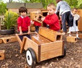 Kinder laden Bausteine in einen kleinen Holzschubkarren mit zwei R&#228;dern und transportieren sie