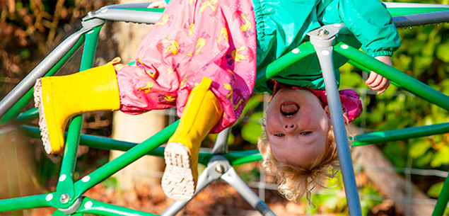 two-year-old girl hanging upside down on climbing frame