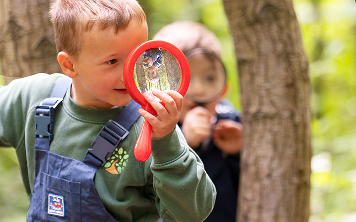 Zwei kleine Jungen erkunden mit einer Lupe die Natur in einem Waldgebiet