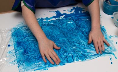 Ein Kind bedeckt ein Blatt Papier mit nasser Farbe mit Frischhaltefolie