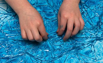 Kinderhände, die ein Stück Frischhaltefolie auf einem Blatt Papier mit nasser Farbe hochziehen