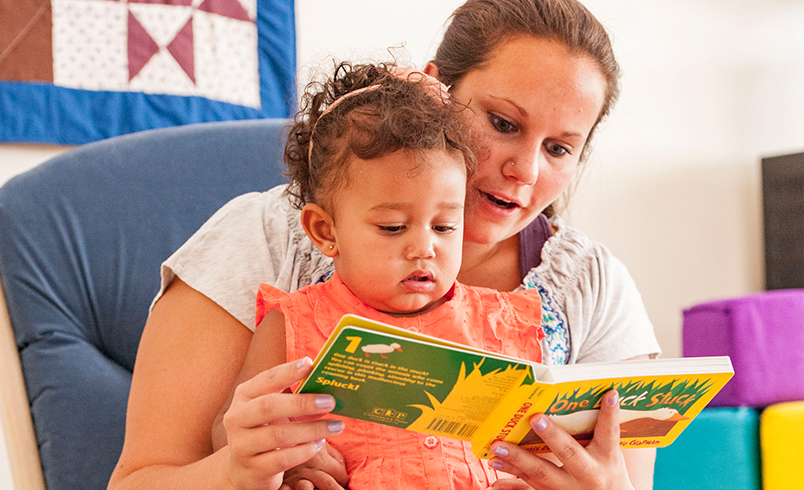 Eine Erzieherin liest einem Kleinkind ein Bilderbuch vor