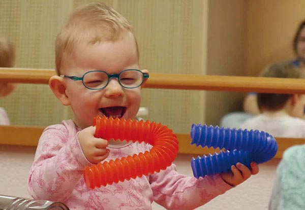 Foto eines Kleinkindes, das mit offensichtlicher Freude mit zwei Kunststoffschläuchen spielt