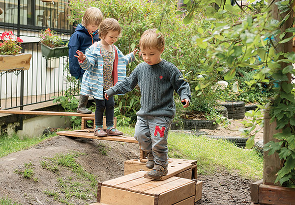 Kinder gehen über eine selbstgebaute Brücke aus Outlast Bausteinen, Brettern und Kästen, hergestellt aus Accoya(R)