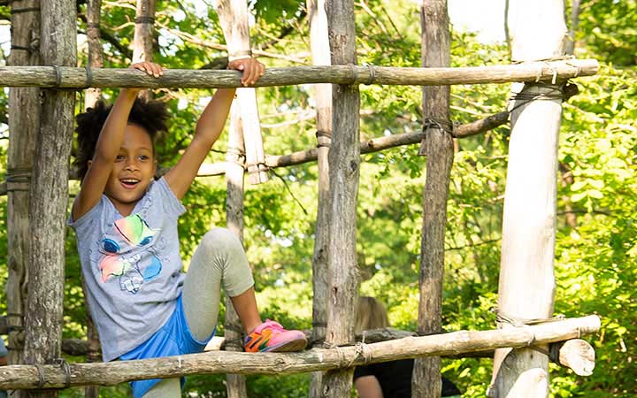 Ein Kind klettert auf einem natürlichen Klettergerüst aus Holz im Freien