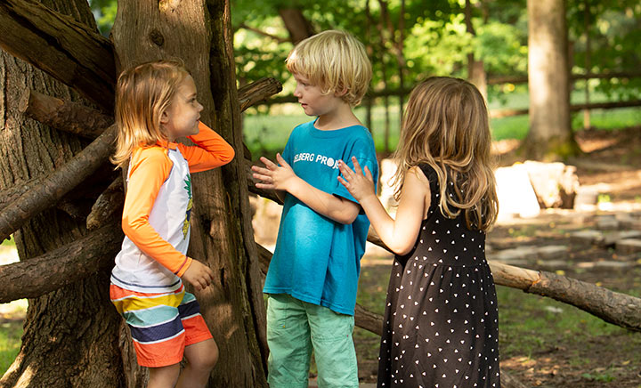Drei Kinder stehen bei einem Baum und reden miteinander