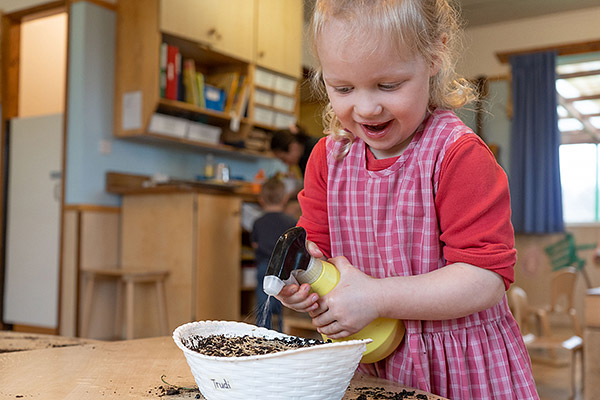 Mädchen besprüht Grassamen mit Sprühflasche