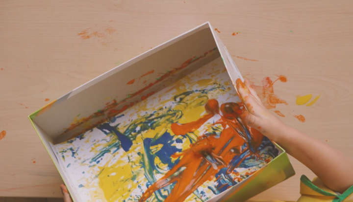 Kind rollt orangefarbene Eicheln über Papier in einem Karton