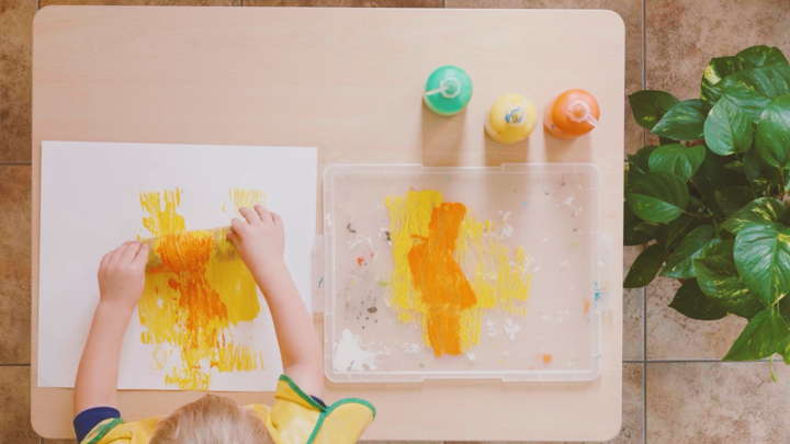 Ein Kind rollt Farbe auf Papier mit Hilfe eines mit Schnur umwickelten Papprohrs