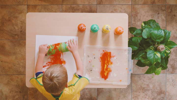 Kind benutzt mit Schnur umwickelte Pringles-Dose, um Farbe auf Papier zu rollen