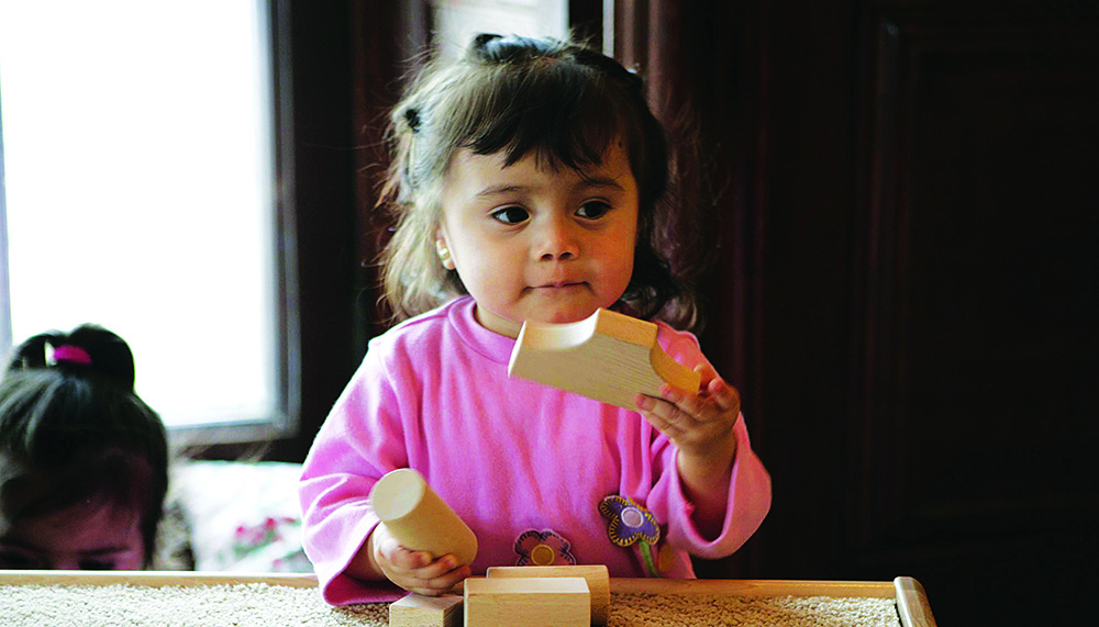 Ein kleines Mädchen experimentiert an einem Tisch mit Holzbausteinen