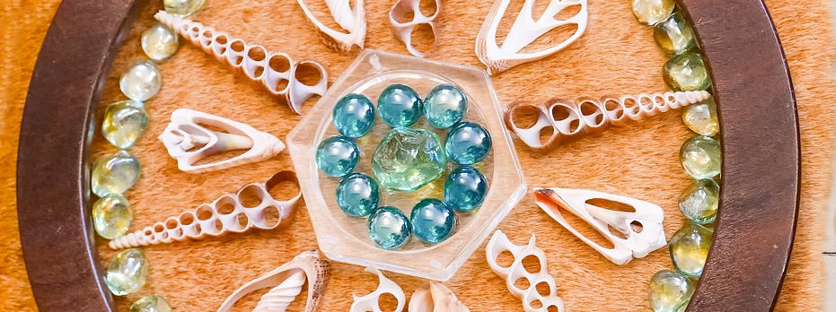Glasmurmeln, Muscheln und andere Materialien, angeordnet in einem runden Holzrahmen