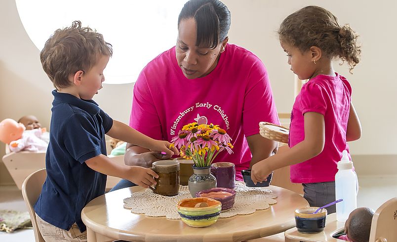 Erzieherin sitzt am Spieltisch mit 2 Kindern
