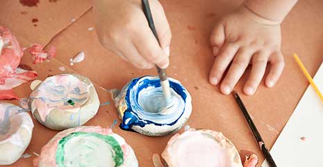 Eine Kinderhand hält einen Pinsel und taucht ihn in einen Farbtopf.