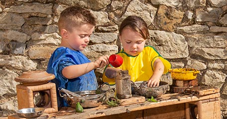 two small children playing in a mud kitchen