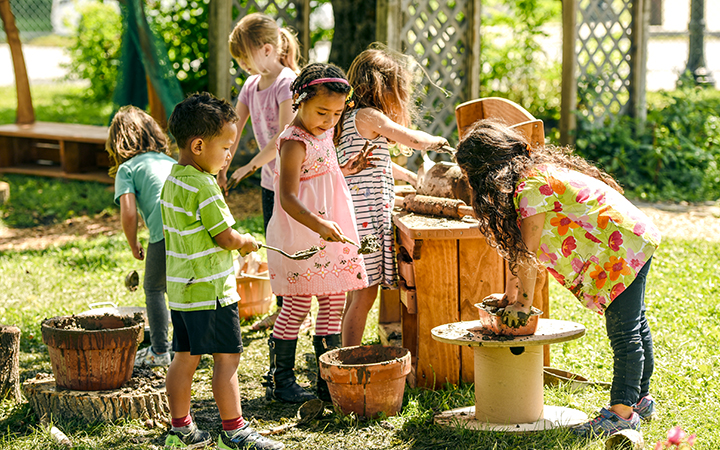 Kinder, die in einer Matschküche im Außenbereich mit Matsch spielen.