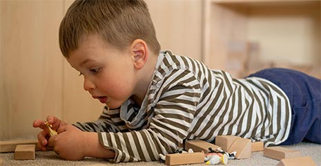 Toddler lying on his tummy playing with small wooden blocks