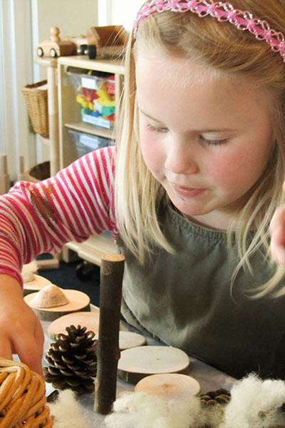 ein kleines Mädchen spielt an einem Tisch mit natürlichen losen Teilen