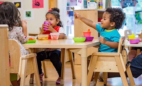 Drei Kinder, die zum Essen um einen Tisch herum sitzen