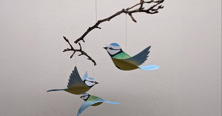 Drei Blaumeisen aus Papier hängen an Ästen