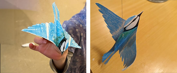 Der fertig gebastelte Vogel aus Papier, einmal in der Hand eines Kindes, einmal an einer Schnur