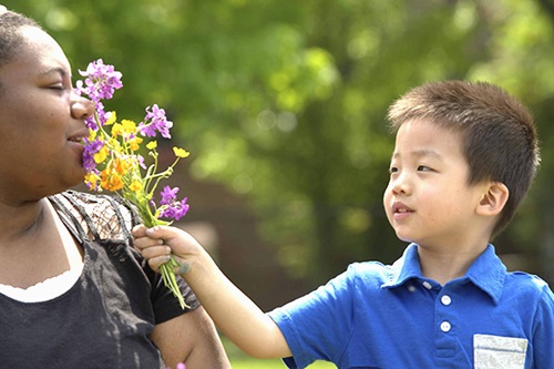 Ein Junge streckt einer Erzieherin Blumen entgegen, damit sie daran riechen kann