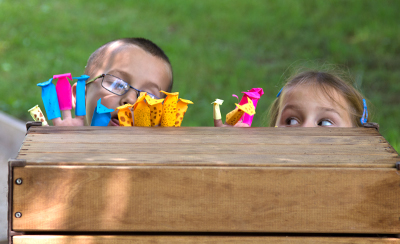 Zwei Kinder verstecken sich hinter einem Outlast Kasten und spielen Puppentheater mit selbst gebastelten Fingerpuppen