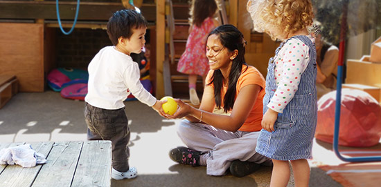 Erzieherin und Kind spielen zusammen mit einem Ball