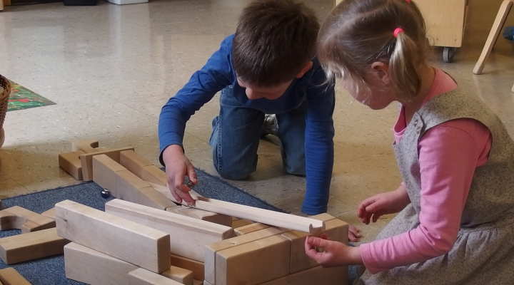 Zwei Kinder rollen eine Murmel eine selbst gebaute Murmelbahn hinunter