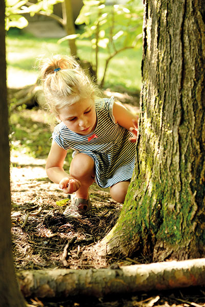 Ein kleines Mädchen untersucht draußen in der Natur Erde und Baumwurzeln