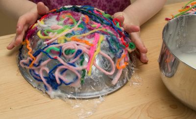 Kinderhände tragen das in Kleister getränkte Garn auf die Schüssel auf