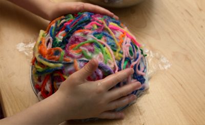 Kinderhände tragen das in Kleister getränkte Garn auf die Schüssel auf 2