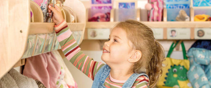 Ein kleines Mädchen greift nach seiner Brotdose auf einer Garderobenablage