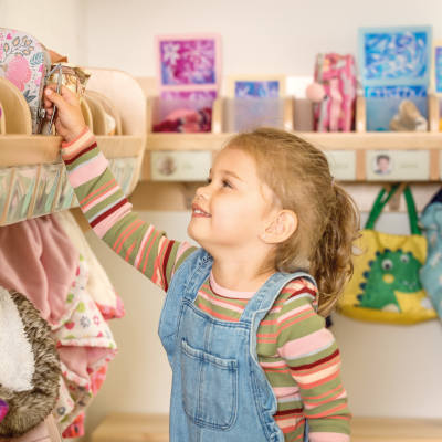 Ein kleines Mädchen greift nach seiner Brotdose auf einer Garderobenablage