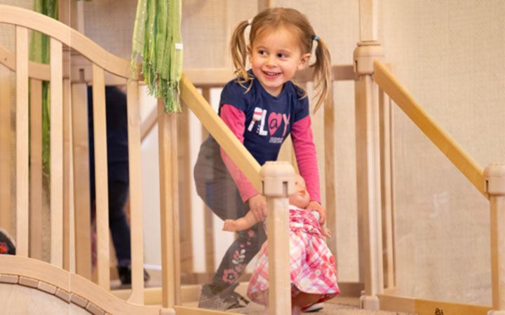 Happy five year old girl playing with doll on Nursery gym