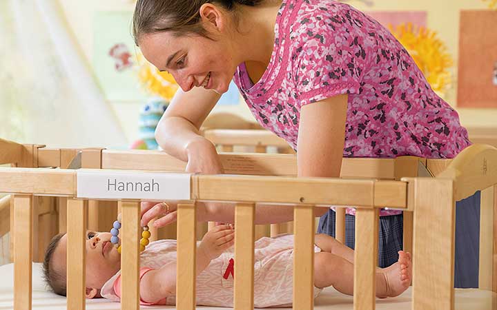 A nursery teacher plays with a baby in a cot.