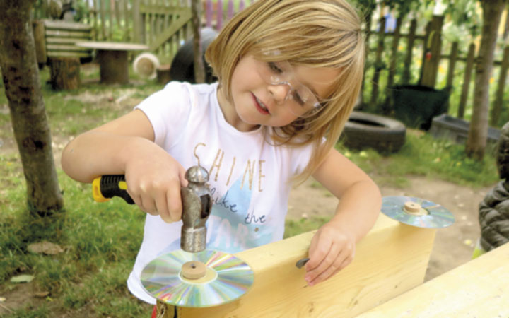 A young girl hammering a CD onto her woodwork creation