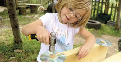 A young girl hammering a CD onto her woodwork creation