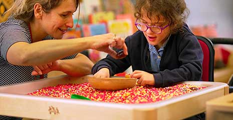 A teacher and a child with SEND do a sensory play activity on a discovery tray table