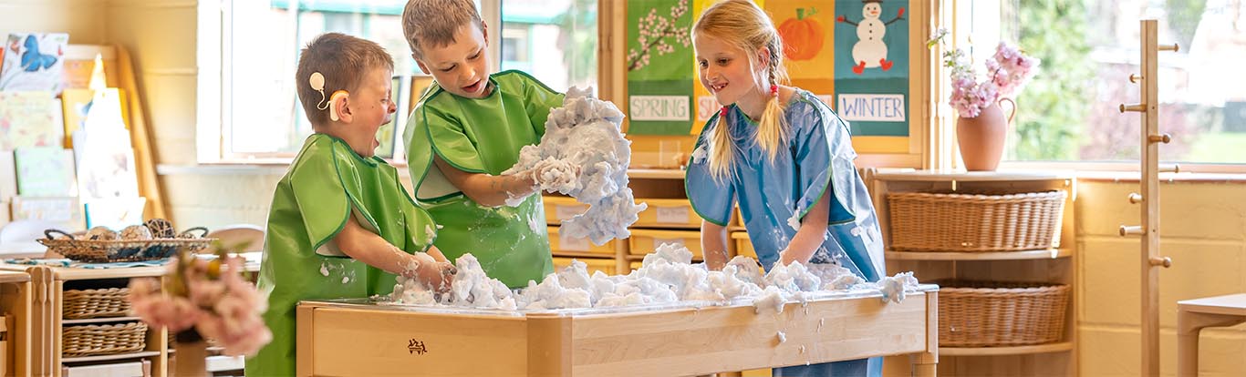 Three children wearing aprons and making a mess with foam