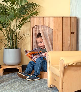 Toddler boy with jeans and green shirt sitting in a Hollow Nook and reading a book.