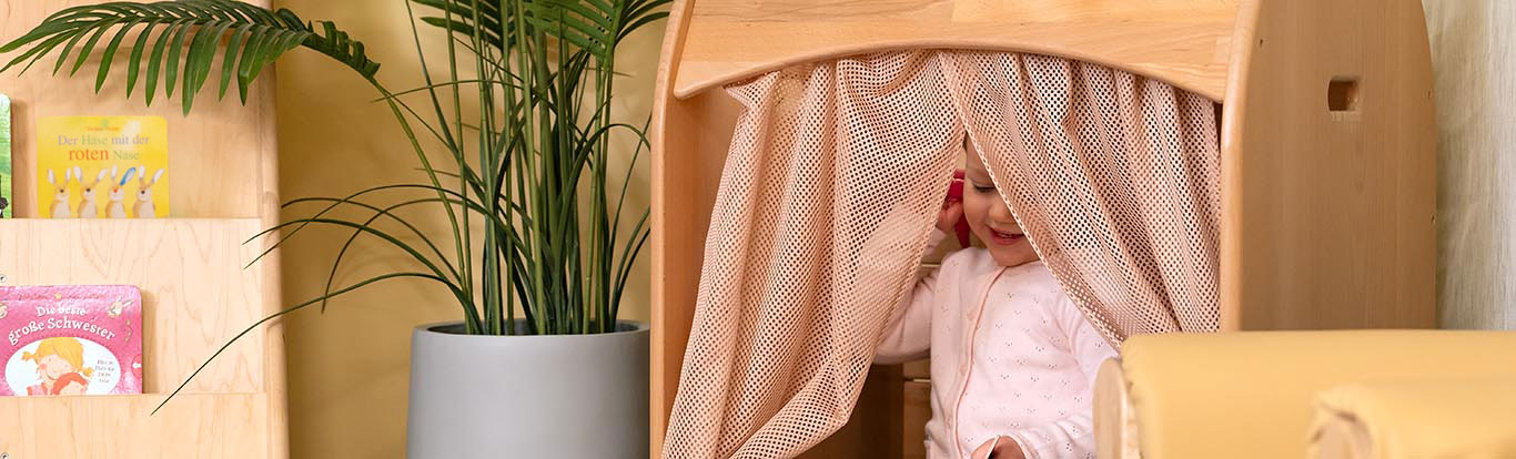 Kleines Mädchen mit rosa Strickjacke, das hinter dem Netzgewebe einer Biberburg sitzt