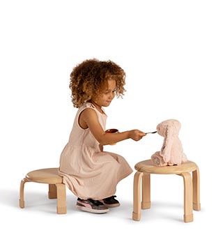 Ein auf einem Stapelhocker sitzendes Kind benutzt einen zweiten Hocker als Tisch