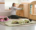 Two children sleeping on rest mats with a teacher putting more mats away into a cupboard