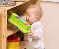 baby wearing white and pink flowered shirt taking toy of solid wood shelf