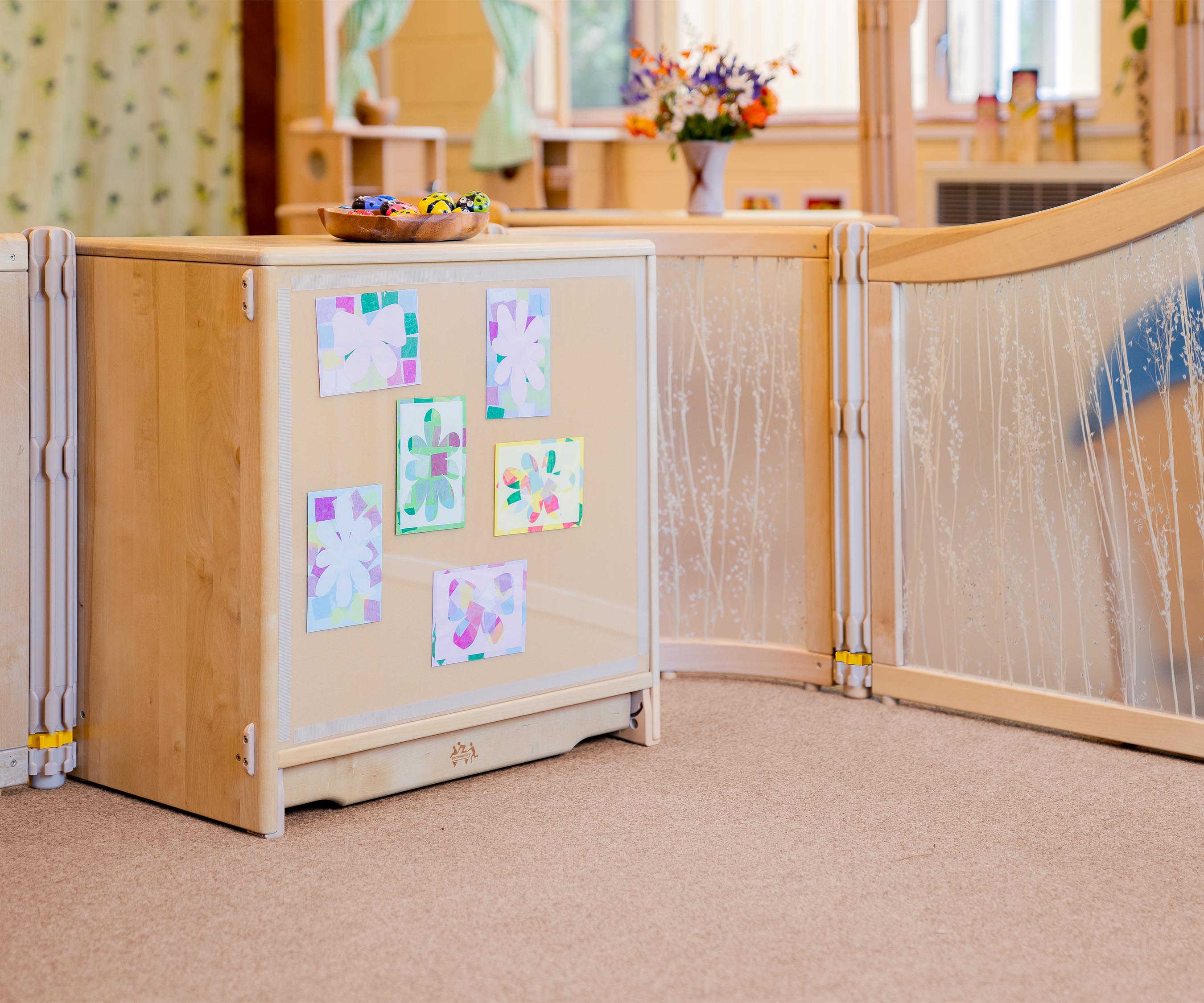 A solid wood school and nursery storage shelf with a clear cover on the back protecting childrens paper mosaics.
