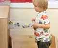 Boy wearing dinosaur shirt pulling clear drawer out from solid wood shelf
