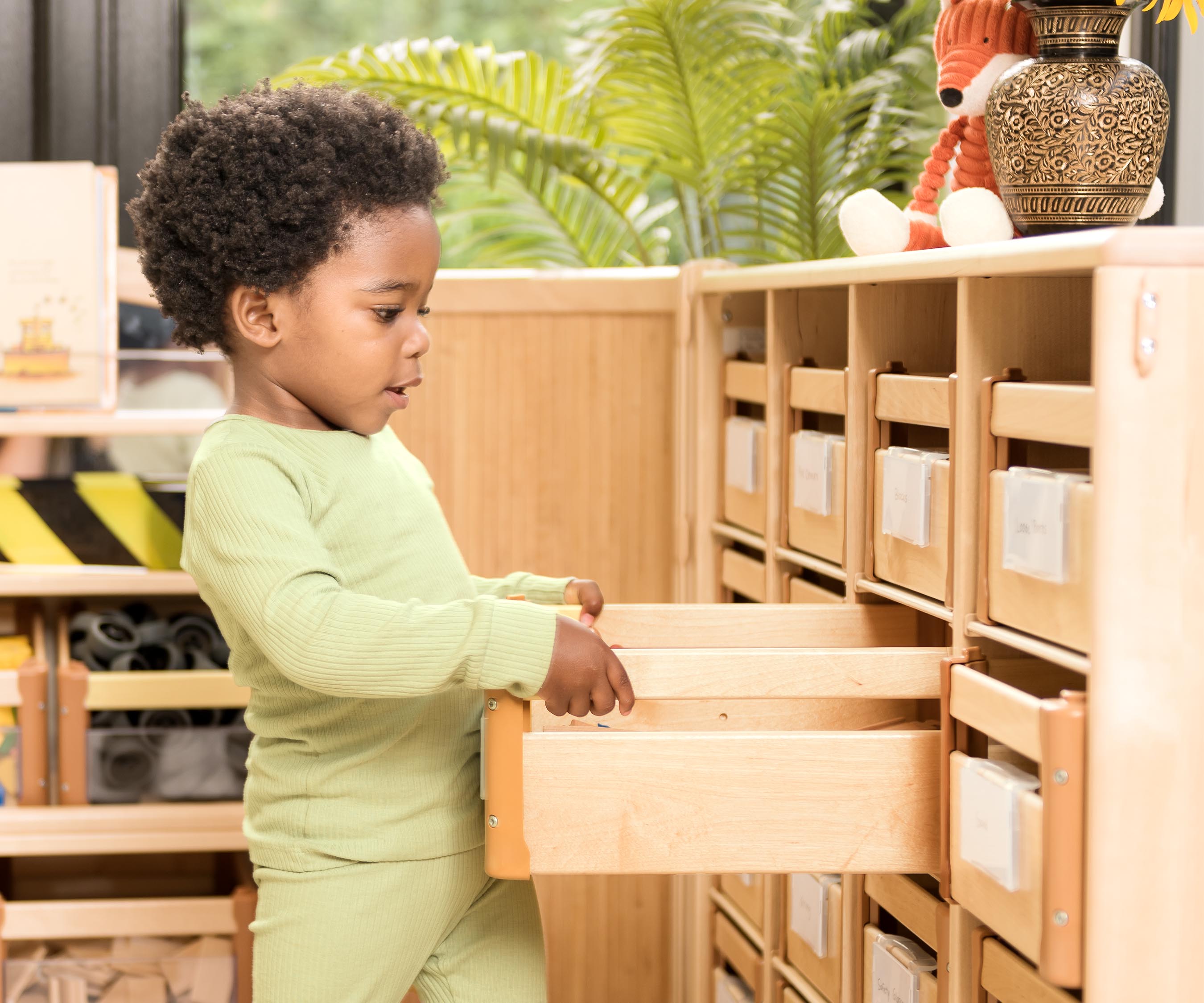 Junge im grünen Spielanzug, der einen Holzkasten aus dem Regal zieht