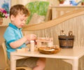 Nursery aged boy wearing aqua shirt sitting at table and playing with small wooden blocks and loose parts
