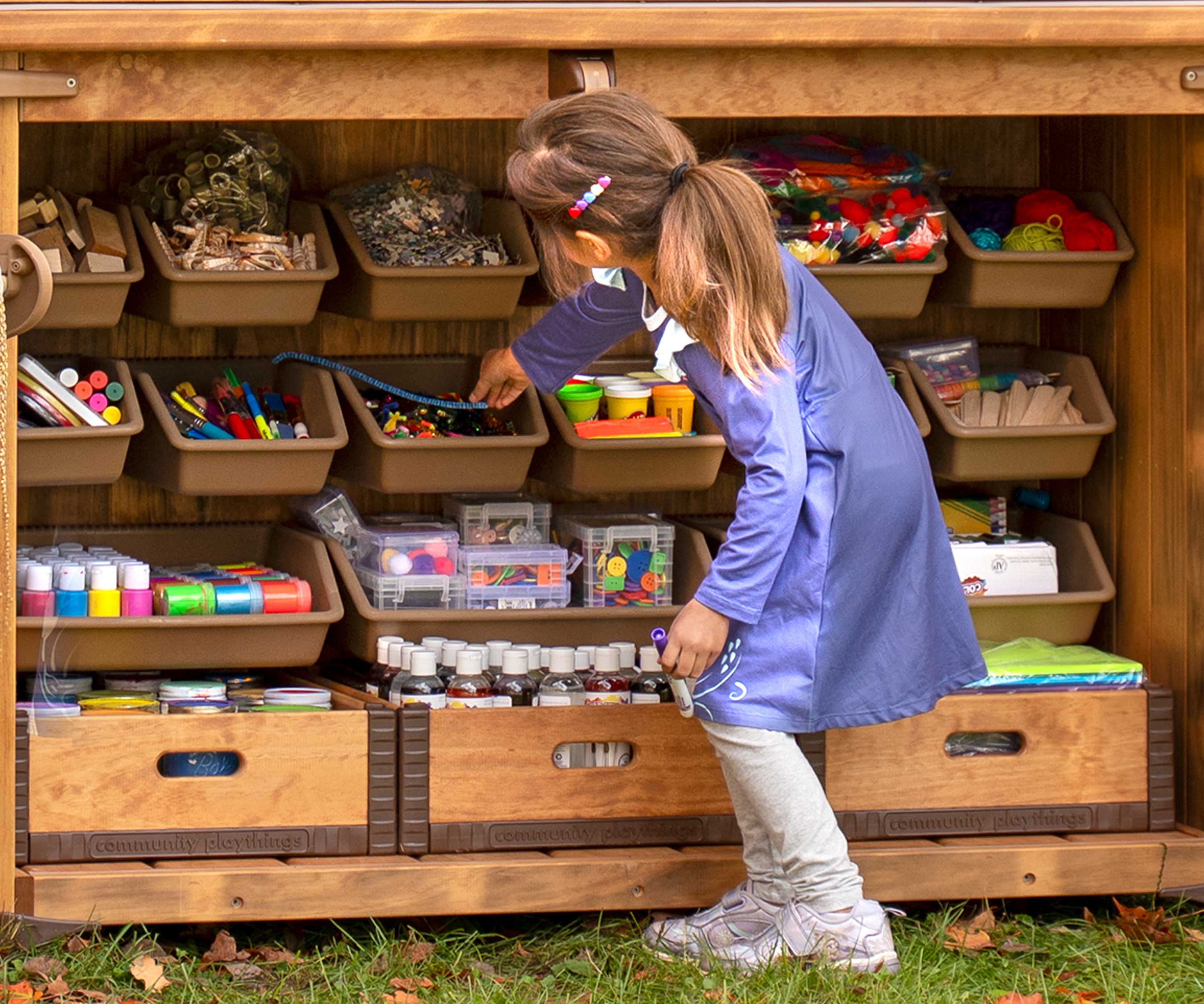 Ein Mädchen, das Materialien aus einem im Freien stehenden Kunstlagerraum auswählt, der mit vielen Behältern organisiert ist.